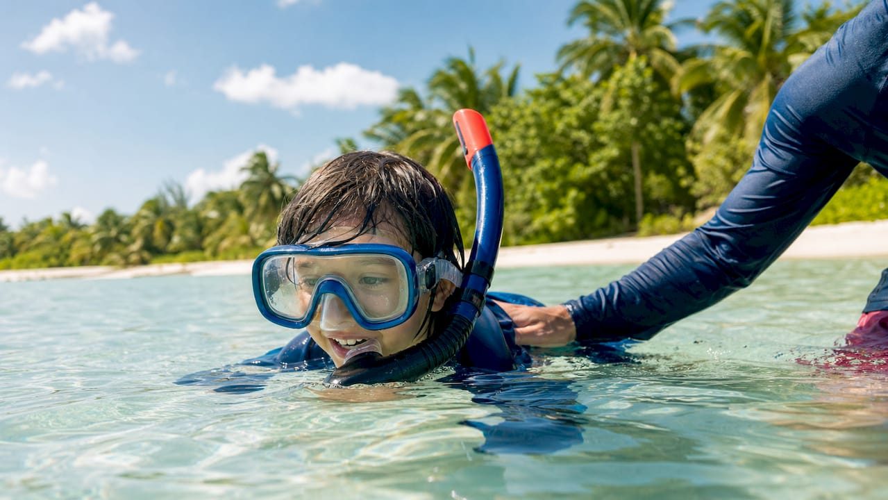 Child snorkeling with traditional mask and adult support