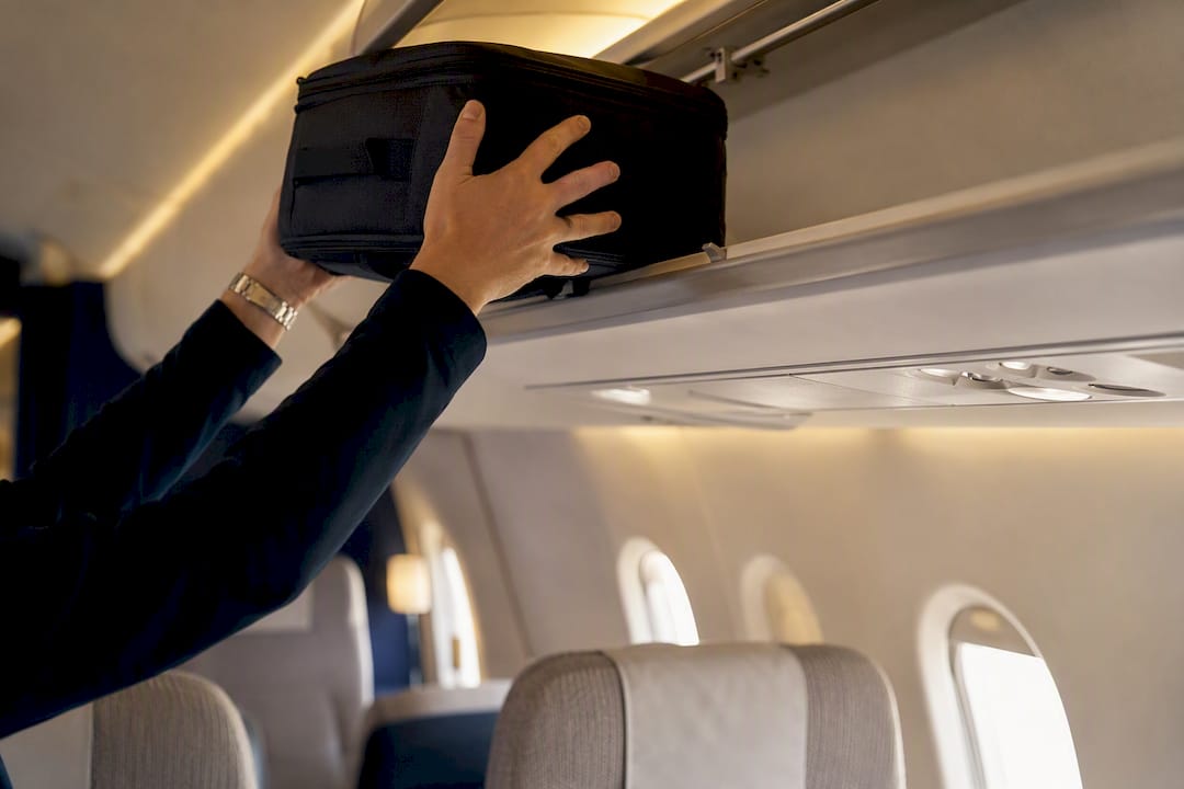 Hands stowing carry-on luggage in airplane bin