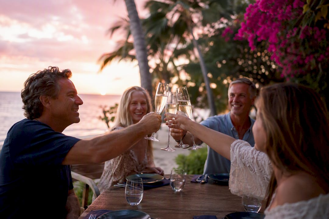 Hands toasting with champagne on Caribbean beach at sunset